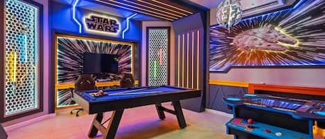 A room with a pool table, a Star Wars-themed wall, and a pinball machine.
