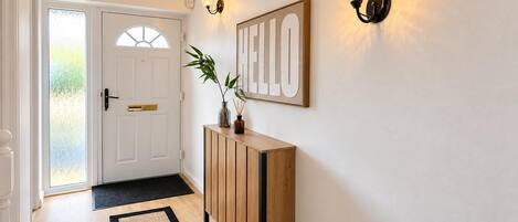 A hallway with a wooden console table, a 'HELLO' sign, and a door with frosted glass panels.