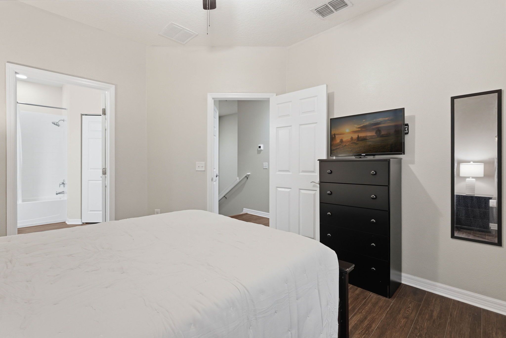 A bedroom with a bed, a dresser, a television, and a bathroom door.