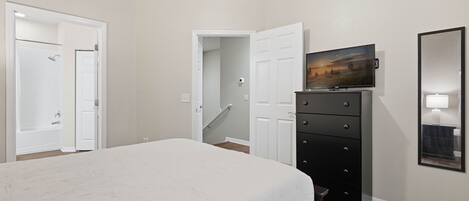 A bedroom with a bed, a dresser, a television, and a bathroom door.