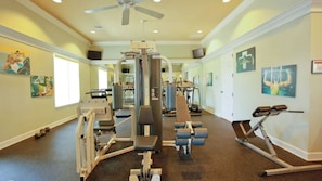 Ett gym med olika typer av träningsredskap, en takfläkt och konstverk på väggarna.