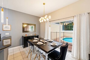 A dining area with a table set for four, a modern chandelier, and a view of a swimming pool. - 4BR Bella Vida Home Near Disney for 11 Guests (Kissimmee)