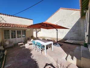 A patio with a table and chairs, an umbrella, and a tiled roof. - Hostcare - La maison du Cadoret - plage nord (Fouras)