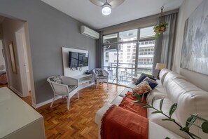 En moderne stue med sofa, fjernsyn og balkon med udsigt til bygninger.