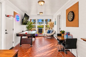 Quarto com mesa de bilhar, dardos e um letreiro neon.