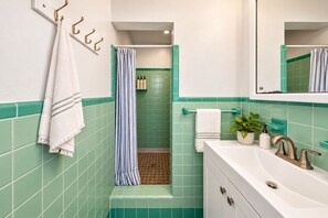 Ein Badezimmer mit grünen Fliesen, einem weißen Waschbecken, einem Spiegel, einem Handtuchhalter und einer Duschvorhang.