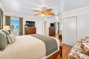 A hotel room with a bed, a ceiling fan, a TV, a dresser, and a floral sofa. - Riverfront Historic | Game Room | Rest A Shore (Port Orange)