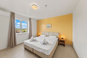 A hotel room with a bed, a window with curtains, a bedside table with a lamp, and a wall-mounted picture. - Blue Bay Ocean View | Luxury 2-Bedroom with Beach Access (Willemstad)