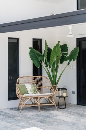 A wicker chair with a cushion and a large plant beside a building with black doors. - This is Casa Valle del Sol where jungle meets the sky. Welcome to your modern luxury retreat with boutique hotel vibes. Located just minutes away from the area's top beaches. Thoughtfully and professionally designed for luxury boutique style comfort. (Matapalo)