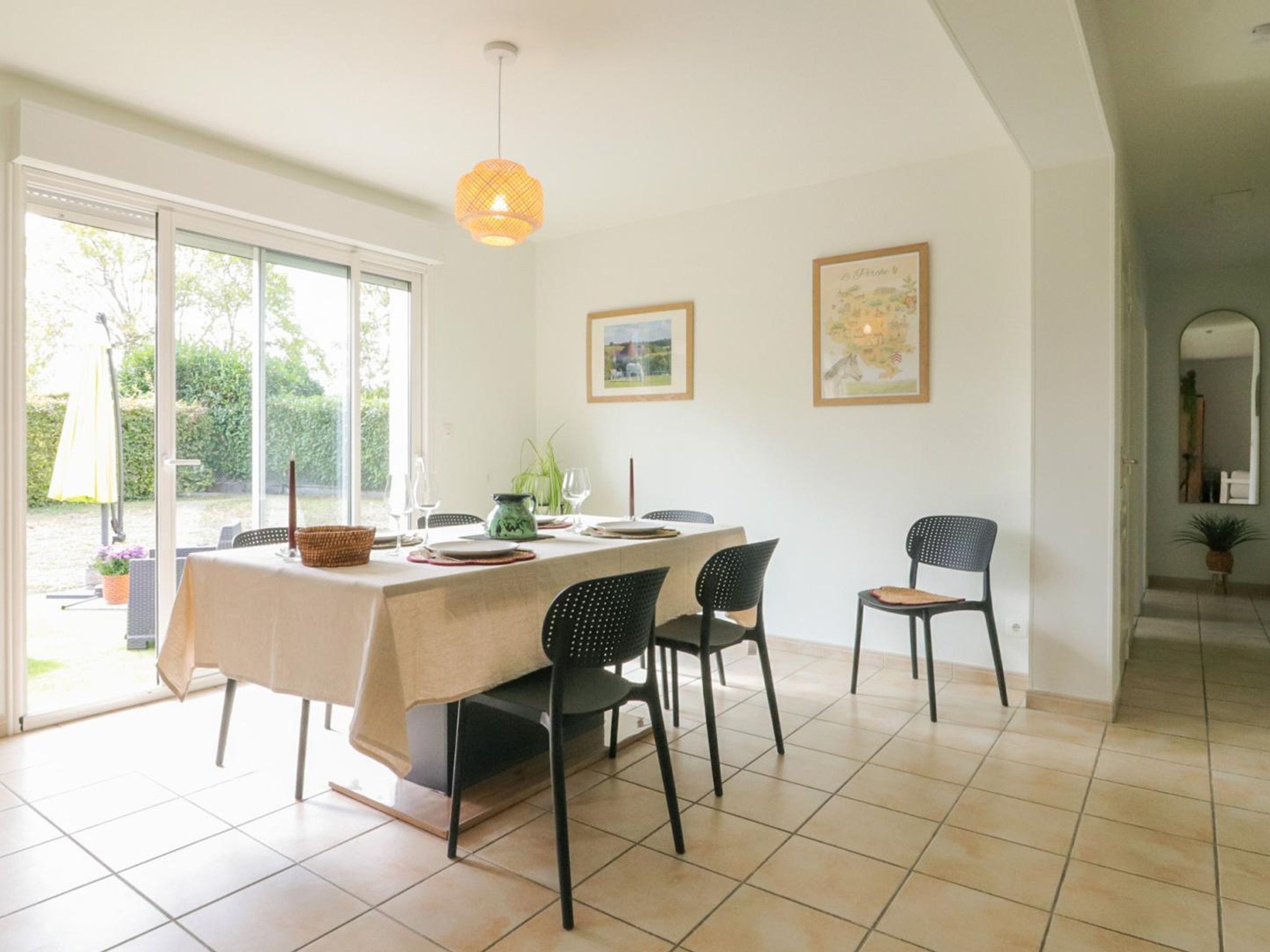 Een eetruimte met een tafel voor vier personen, stoelen, een hanglamp en twee afbeeldingen in lijsten aan de muur.