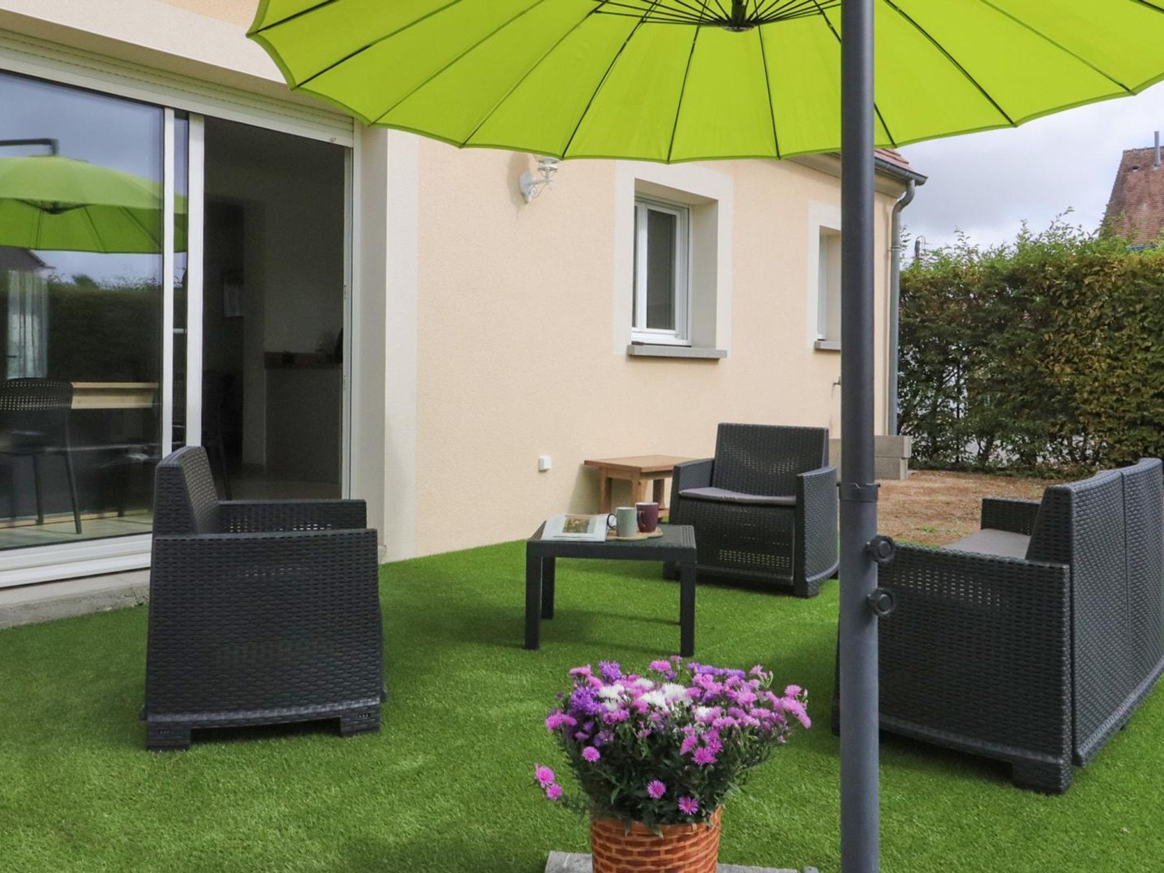 Un espace extérieur aménagé avec des meubles en osier et un parasol vert.