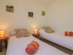 Habitación de hotel con dos camas, cada una con un almohadón y una mesita de noche con lámpara.