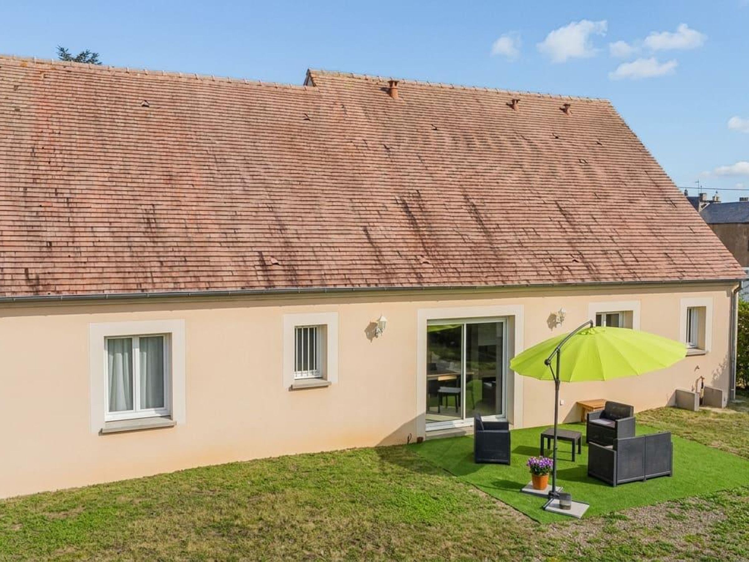 Une maison avec un toit en pente, une terrasse avec des meubles d’extérieur et une pelouse verdoyante.