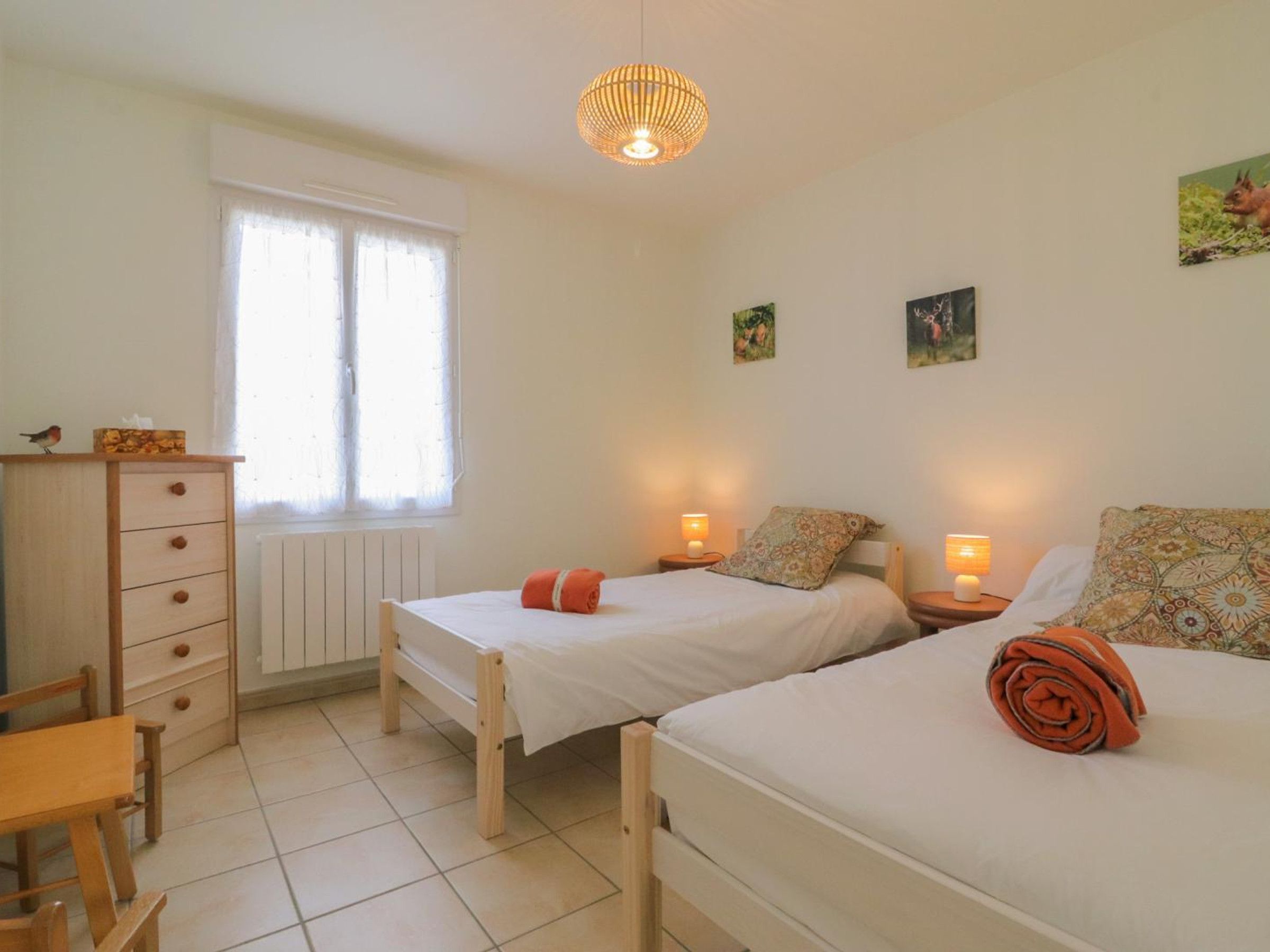 Une chambre avec deux lits simples, une commode en bois, une chaise et une fenêtre avec des rideaux.