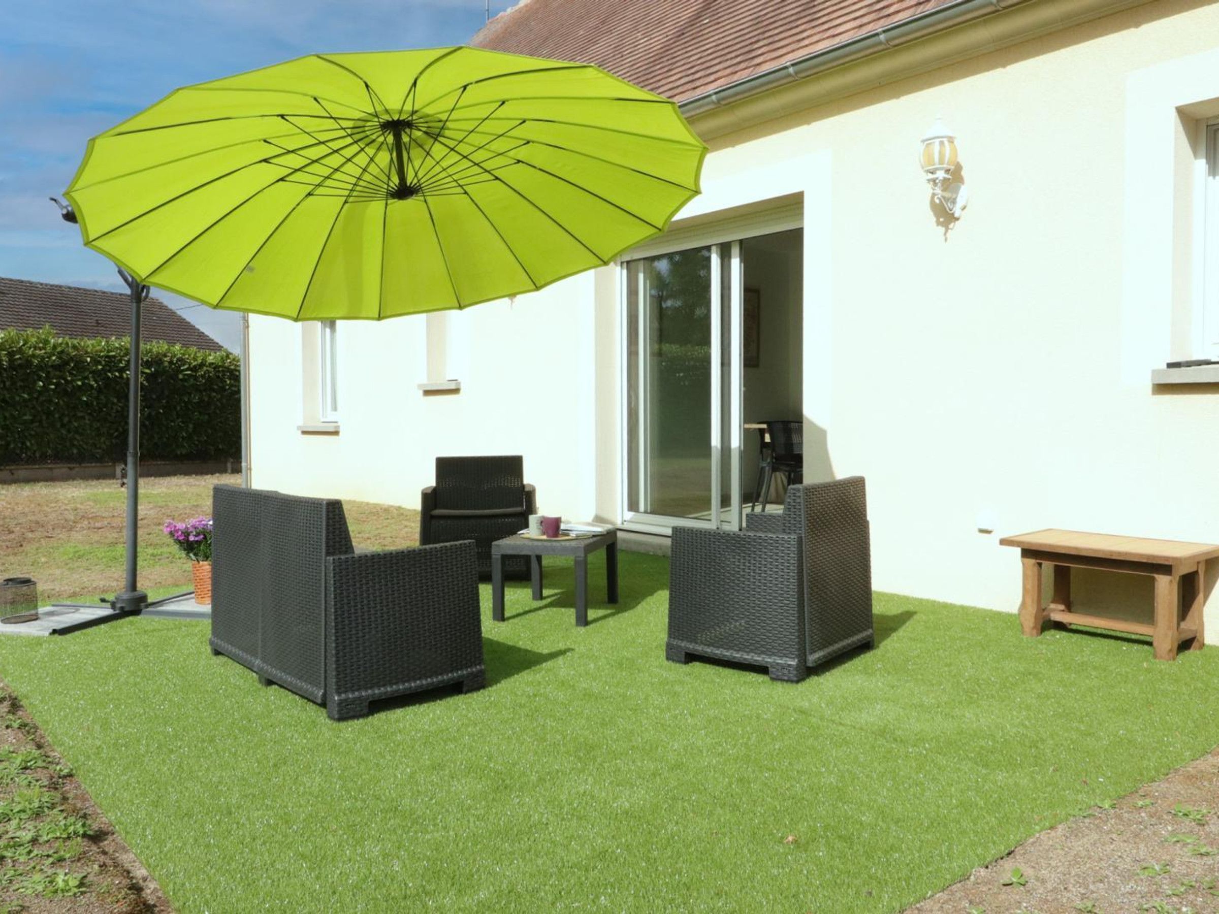 Een terras met kunstgras, twee rieten stoelen, een klein tafeltje en een houten bank.