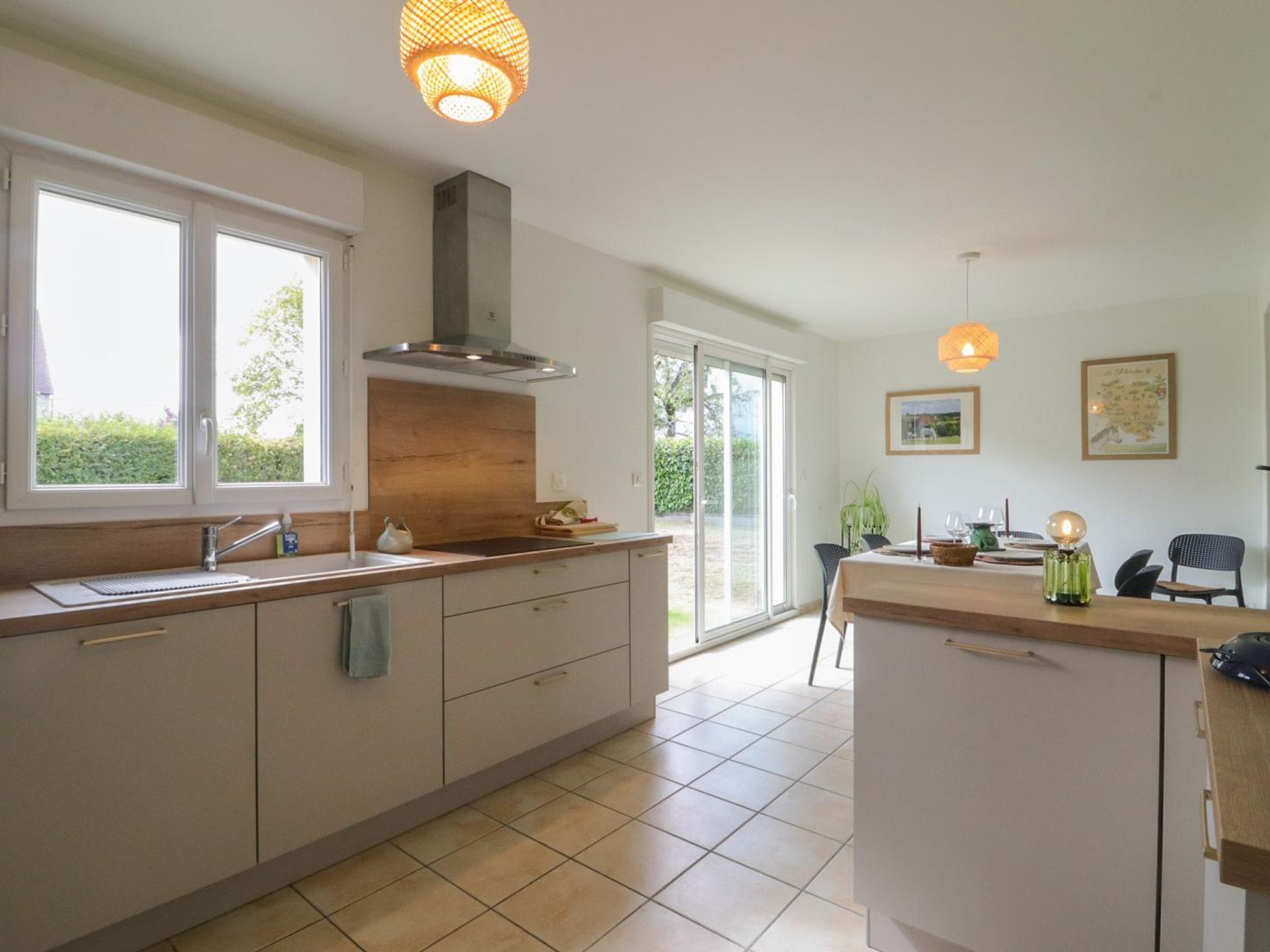 A modern kitchen with a large island, a built-in oven, and a window overlooking a garden.