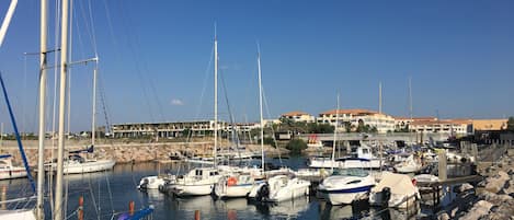 A marina with various boats docked, a rocky shoreline, and a building with multiple balconies in the background.