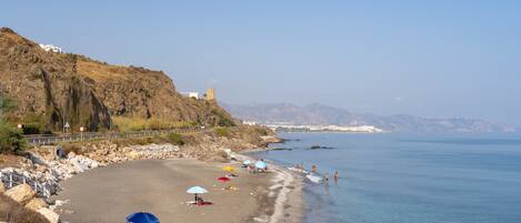 A beach with umbrellas, rocky terrain, and a distant mountain range.