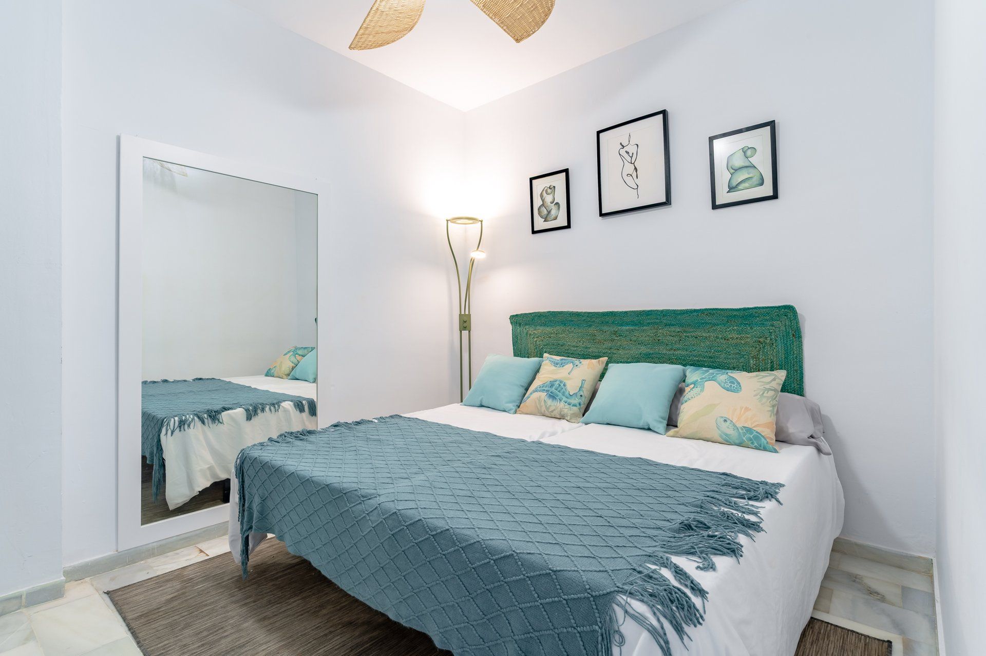 A bedroom with a bed, a mirror, and three framed artworks on the wall.