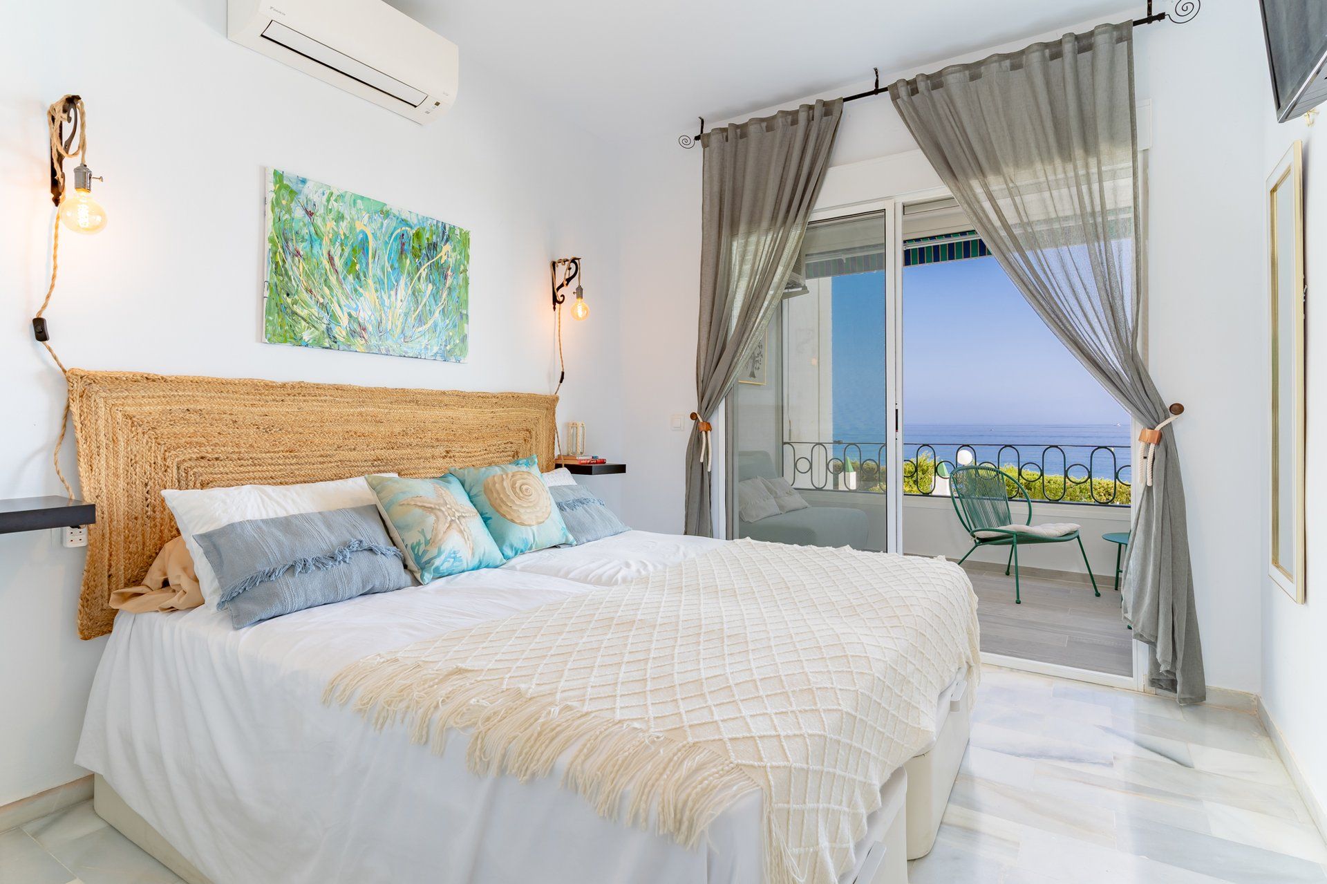 Une chambre avec un grand lit, une vue sur la mer depuis un balcon et un tableau accroché au mur.