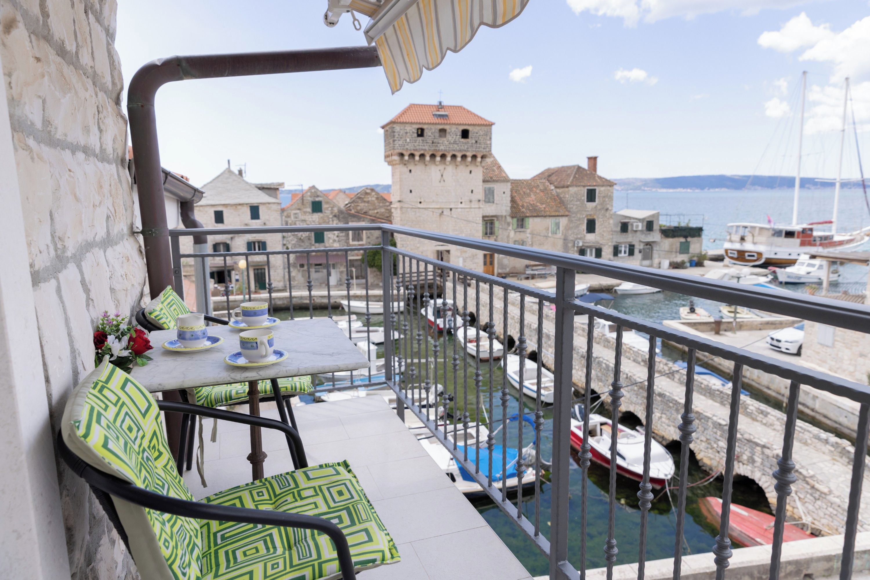 A balcony with a table and chairs, overlooking a marina with boats and historic buildings.