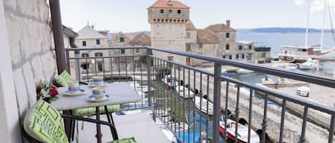 A balcony with a table and chairs, overlooking a marina with boats and historic buildings.