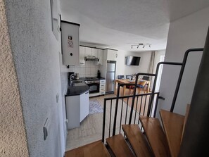 Una cocina moderna con armarios blancos, una estufa y un refrigerador. Hay un comedor con una mesa y sillas.