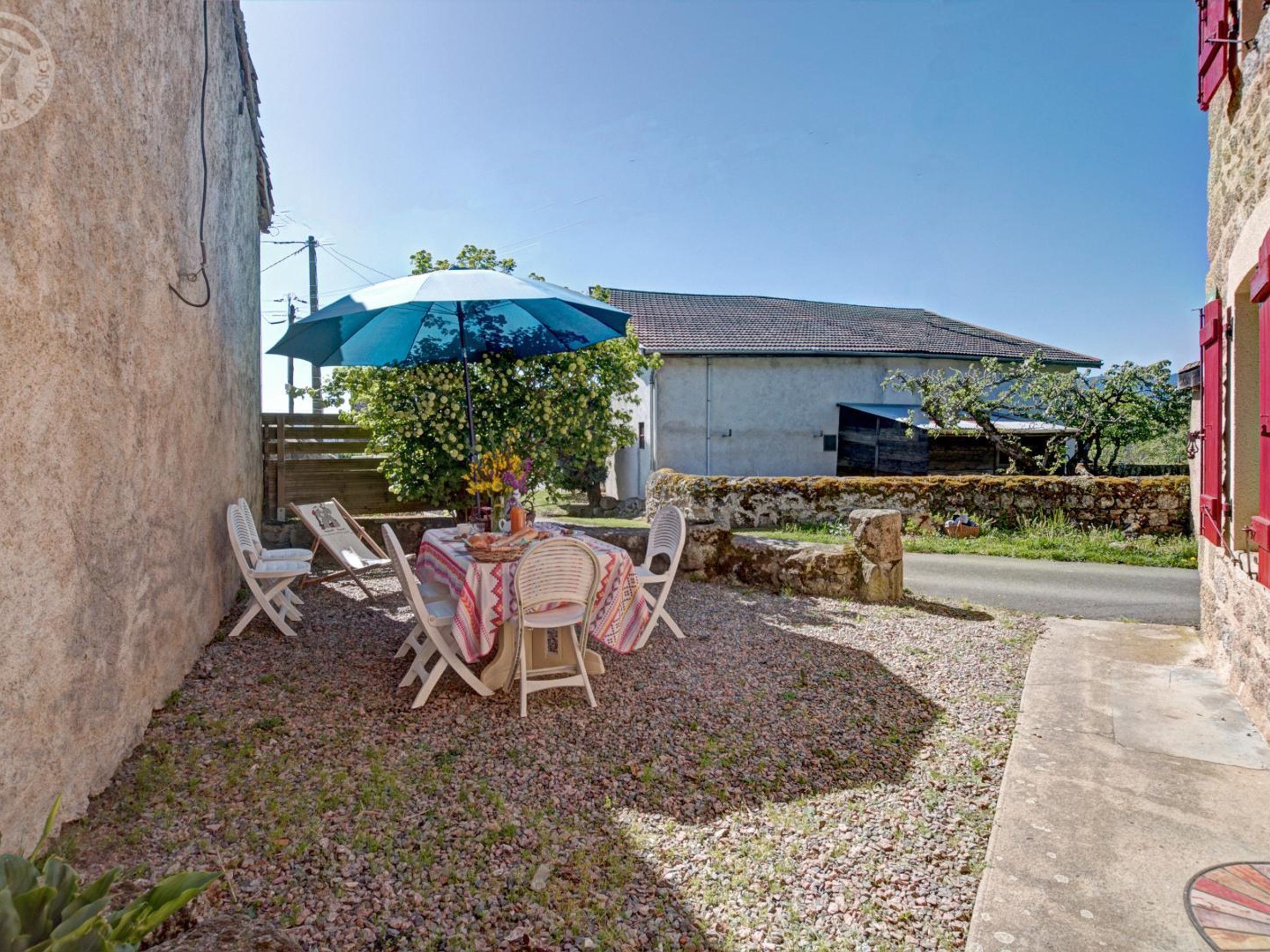 An outdoor seating area with a table and chairs, a blue umbrella, and a stone wall.
