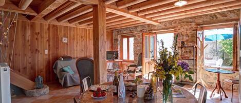 A rustic wooden interior with a dining table set for two, a stone fireplace, and a view of the outdoors.