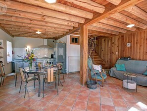 Ein rustikaler Innenraum mit Essbereich, Küche und Wohnbereich, mit Holzbalken, Fliesenboden und einer Couch.