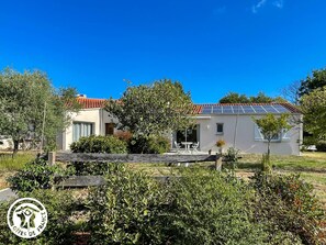 Ein zweistöckiges Haus mit Solardach, kleinem Garten und einer Holzterrasse.