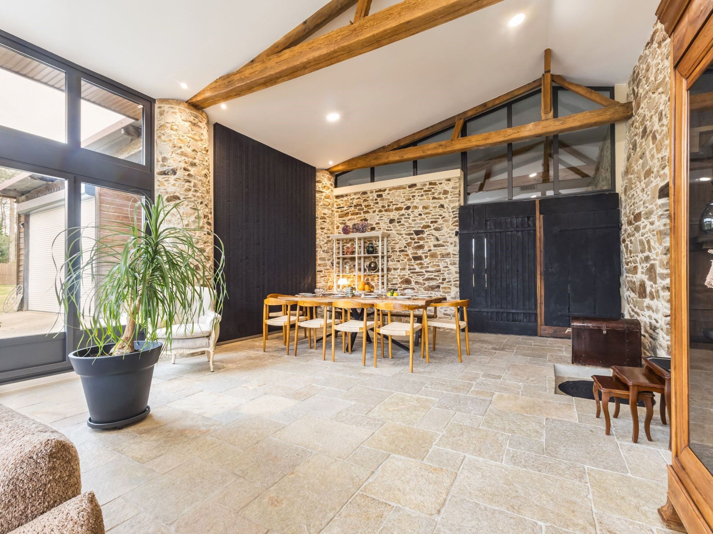Un vaste espace dédié à la salle à manger, avec un mur en pierre, des poutres en bois et une grande fenêtre.