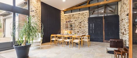 A spacious dining area with a stone wall, wooden beams, and a large window.