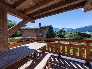 A wooden deck with a table and benches, overlooking a mountainous landscape with houses. - Apartment in Mont d'Arbois - 6 guests (Megève)