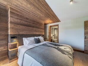 A modern bedroom with a wooden ceiling, a bed with white bedding, a nightstand, and a built-in shelf. - Apartment in Mont d'Arbois - 6 guests (Megève)