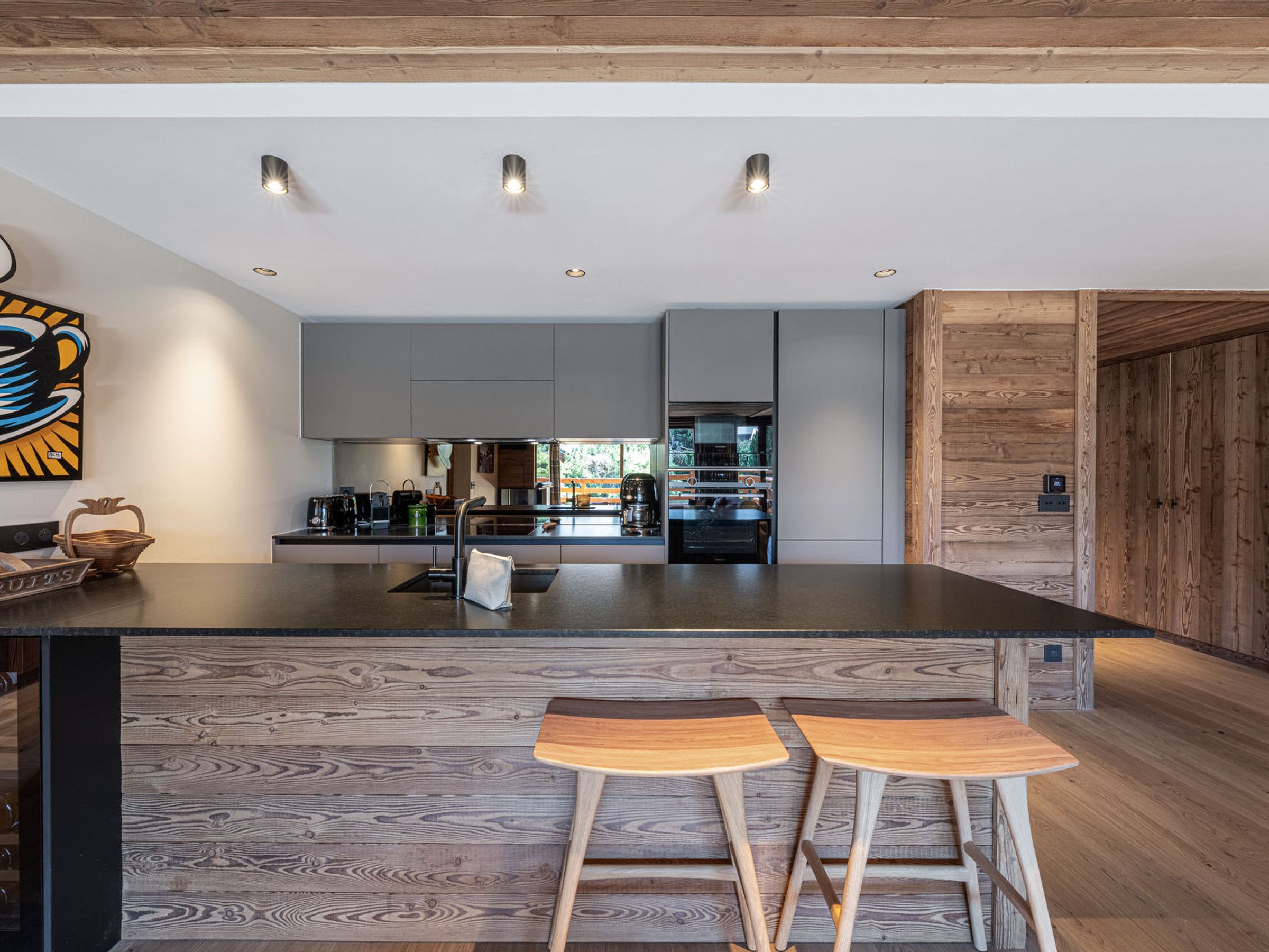 Eine moderne Küche mit Kochinsel, Barhocker und einer Wand in Holzoptik.