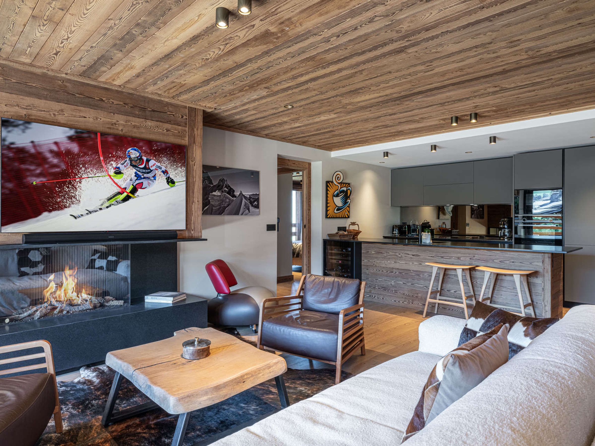 Ein modernes Wohnzimmer mit Kamin, Fernseher und einer Küche im Hintergrund.