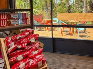 A wooden crate filled with red bags, a wooden bench, and colorful chairs outside a window. - Air-conditioned mobile home - 6 guests (Sainte-Marie-la-Mer)
