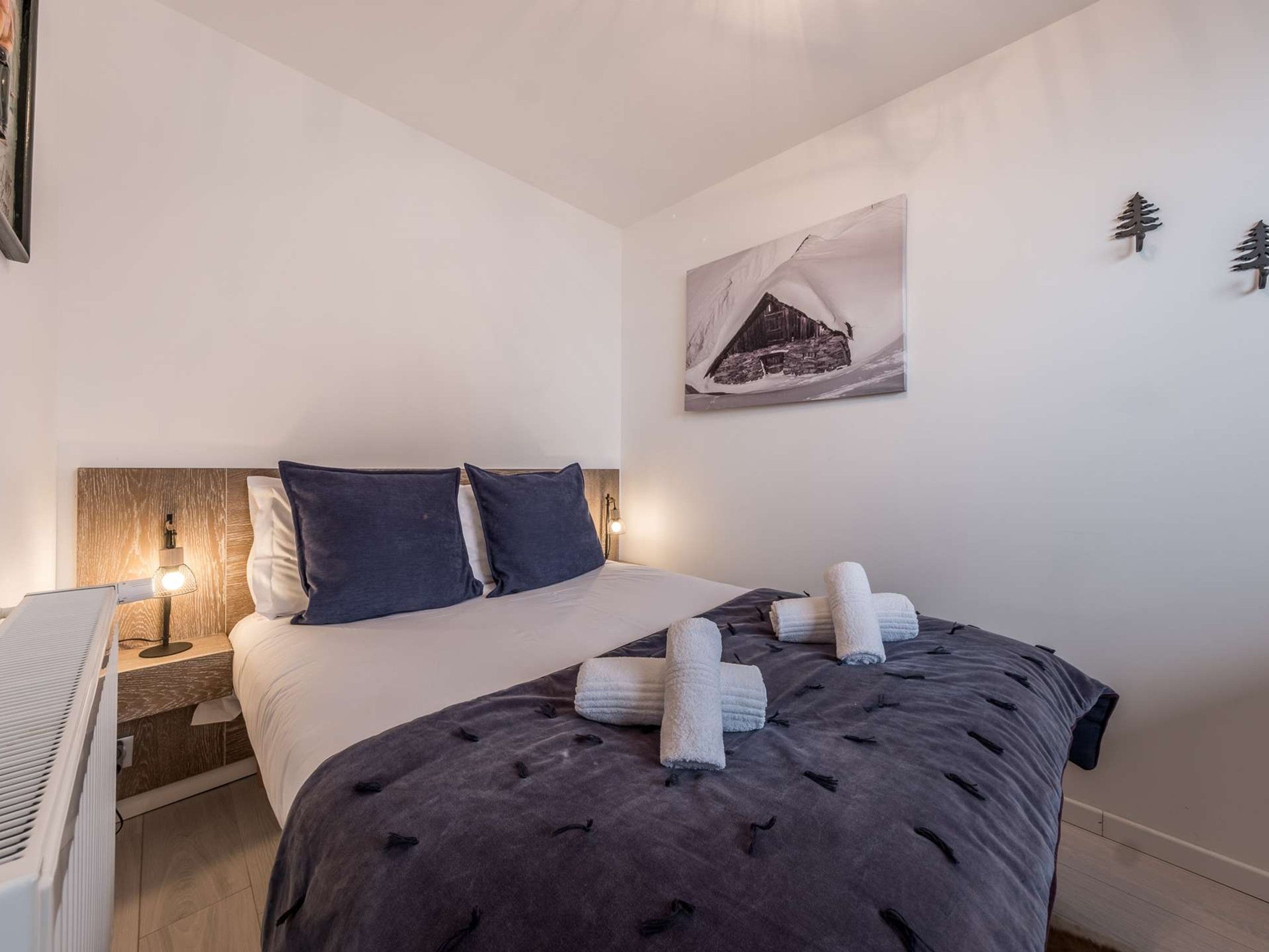 A bedroom with a bed, pillows, a nightstand, a lamp, and a painting on the wall.