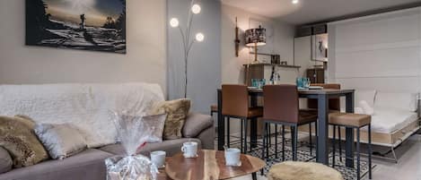 A modern living room with a sofa, coffee table, ottoman, dining table, chairs, and a painting on the wall.