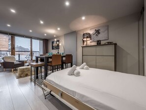 A modern hotel room with a bed, desk, chairs, and a view of the outdoors. - Ski-in/ski-out apartment - 4 guests (Courchevel 1650)