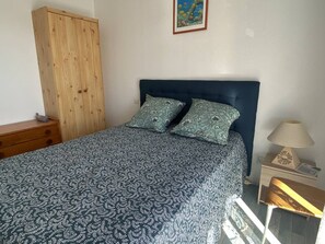 A bedroom with a bed, two pillows, a wooden wardrobe, a nightstand with a lamp, and a framed picture on the wall. - T2 with AC, sea view - 4 guests (Canet-Plage)