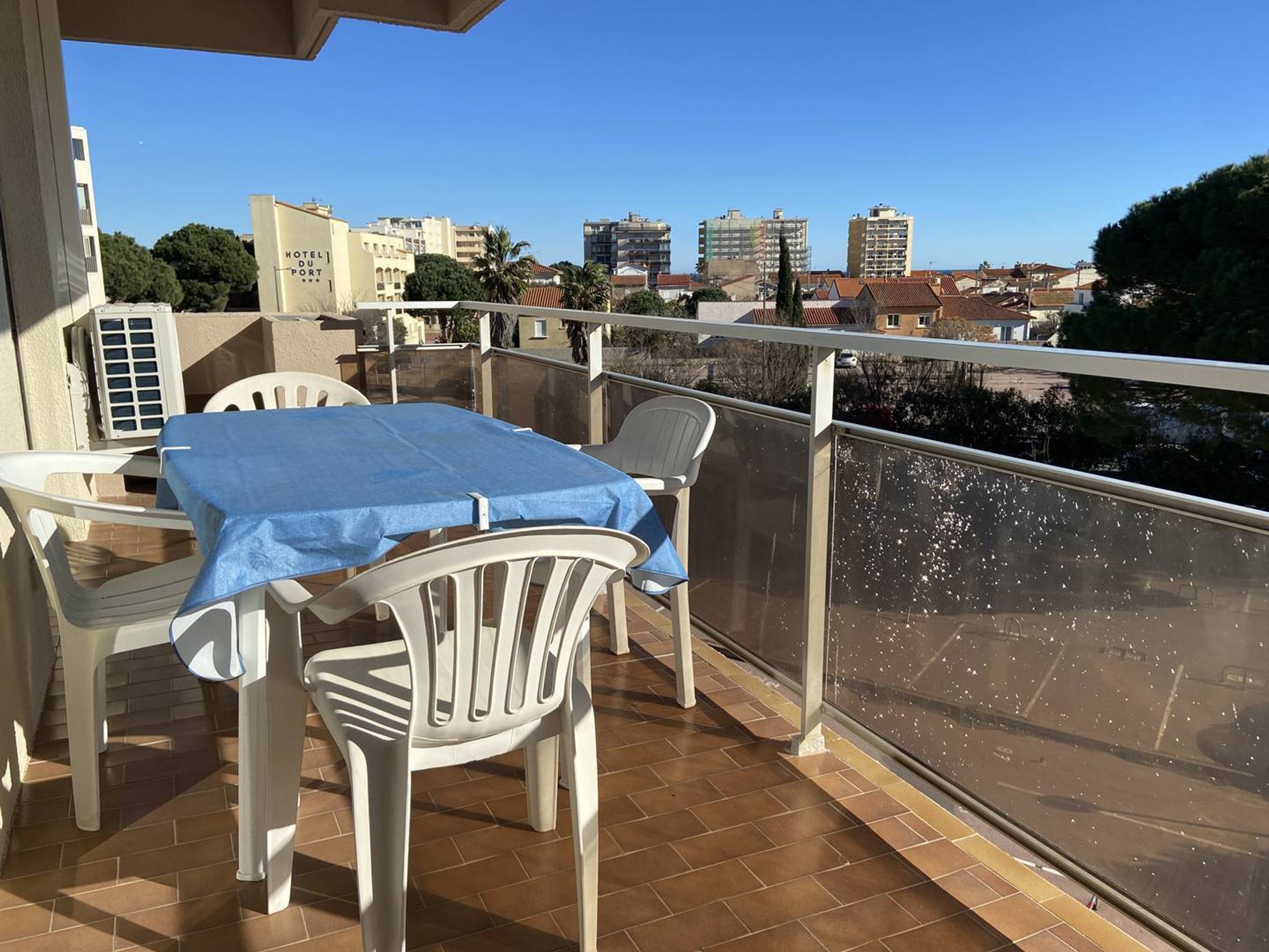 A balcony with a table and chairs, a view of the cityscape, and a building labeled "HOTEL DU PORT".