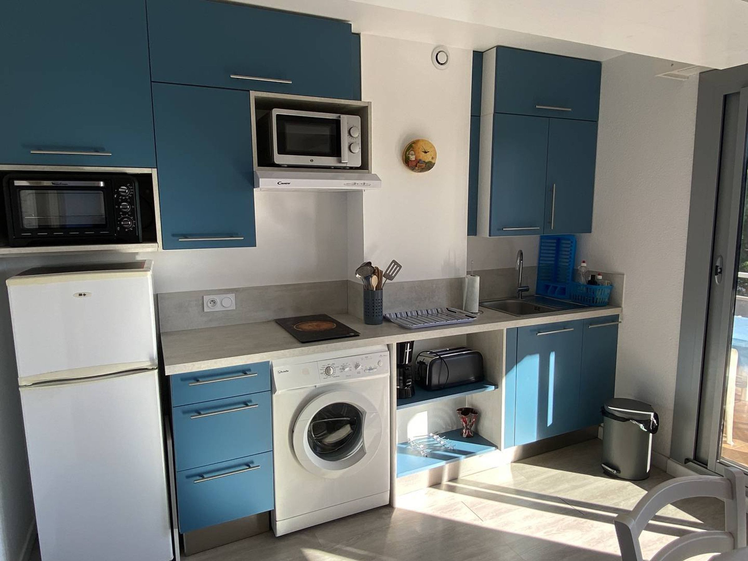 A compact kitchen with a microwave, oven, washing machine, and sink.
