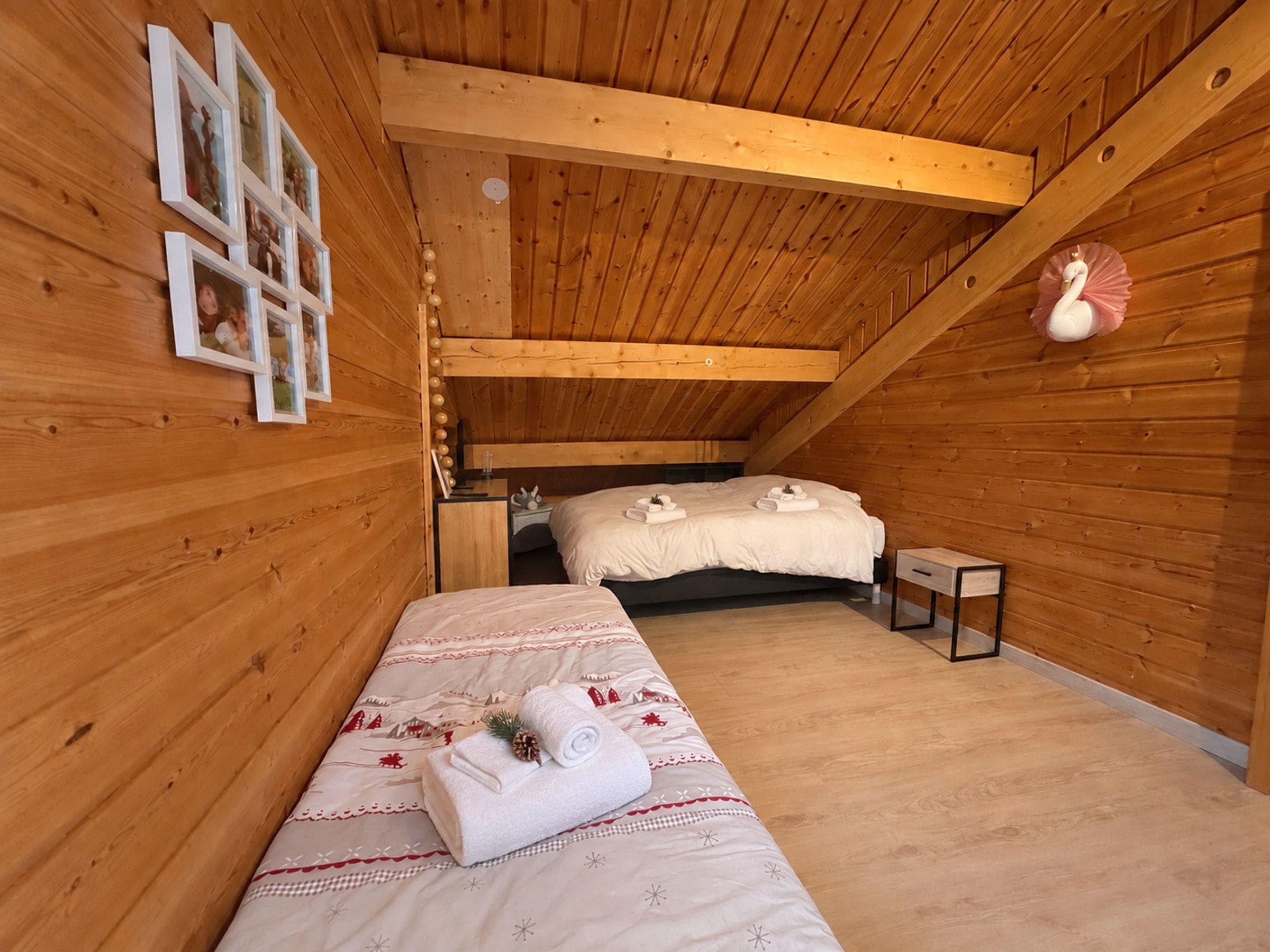 A cozy wooden room with a bunk bed, a small bedside table, and a wall-mounted shelf with framed photos.
