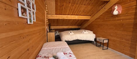 A cozy wooden room with a bunk bed, a small bedside table, and a wall-mounted shelf with framed photos.