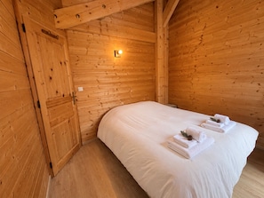 A wooden cabin room with a bed, a nightstand, and a wall-mounted light. - Cozy mountain chalet - 8 guests (Vars)