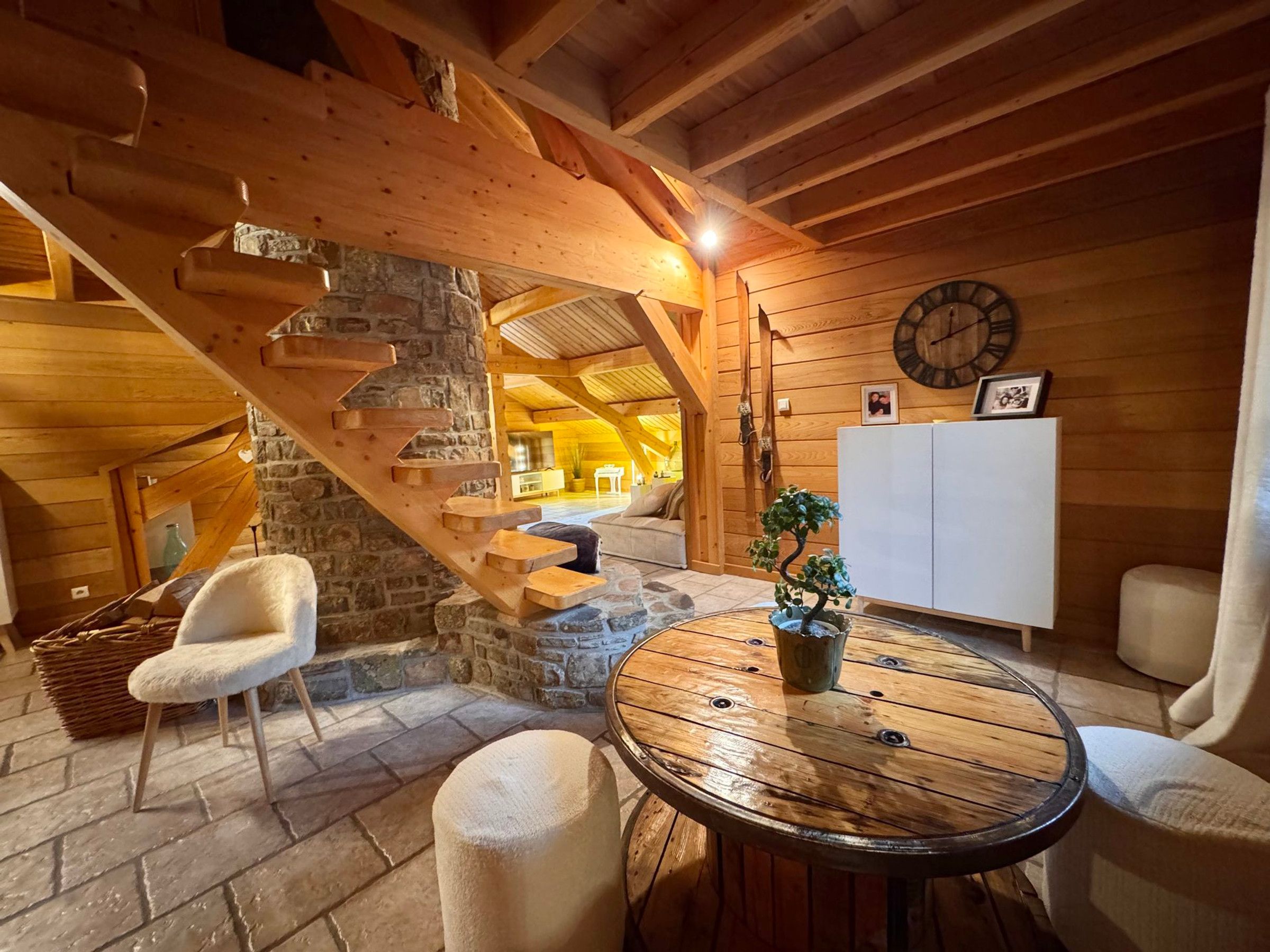 A wooden interior with a stone staircase, a round wooden table, and a white chair.