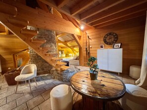 Un interior de madera con una escalera de piedra, una mesa redonda de madera y una silla blanca.