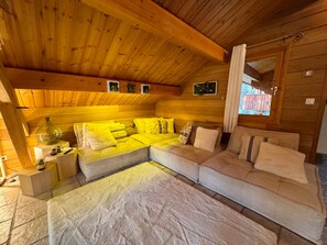 A cozy cabin interior with a wooden ceiling, a sectional sofa, and a small table with a lamp. - Cozy mountain chalet - 8 guests (Vars)